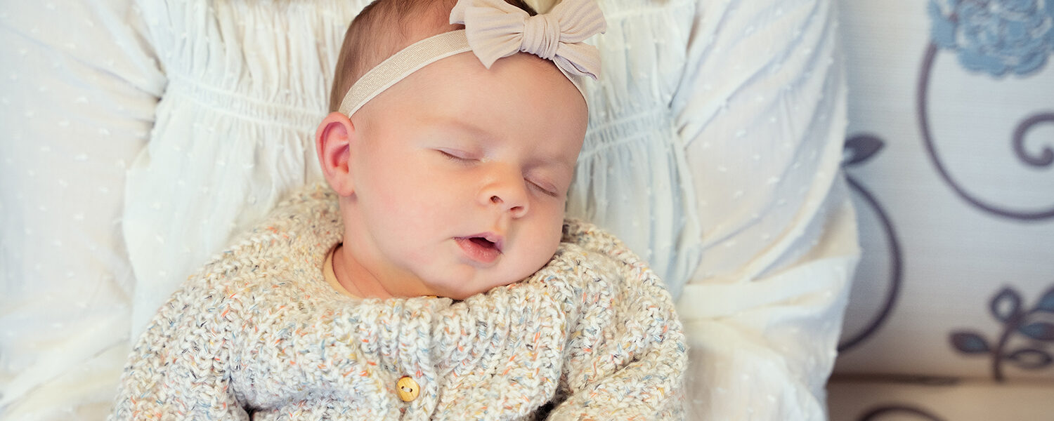 A caucasian baby faces camera, asleep on their mother's lap