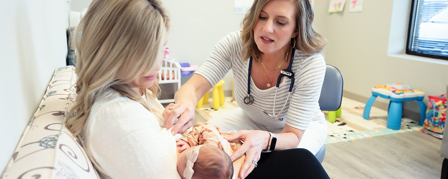 Dr. Beth Galla of Sweetbay Pediatrics places her hands on an infant that is nursing in their mother's arms.